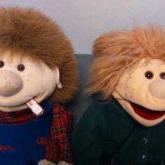 Die Handpuppen Lotti und Willi sitzen nebeneinander und haben einen Schokoriegel im Mund