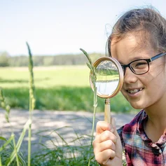 Kind mit Brille sieht durch ein Vergrößerungsglas