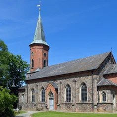 Kirche von rechts, vorn 2 Steige und Laterne links, grüne Eichen beidseitig, im Hintergrund rechts Gutsscheune